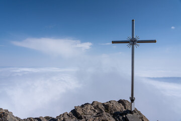 Lonely cross standing on rocky peak above sky full of clouds