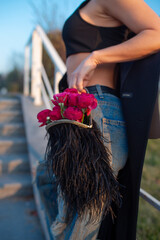 Trendy female look outdoors: feather handbag filled with red roses. Romantic atmosphere.