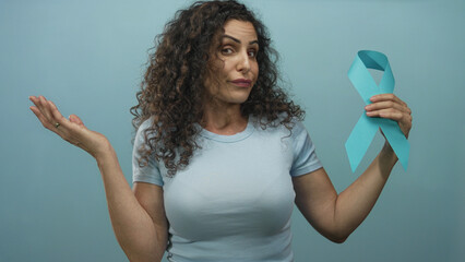 Woman with curly hair holds teal ribbon in studio while inspecting the awareness symbol; hope.