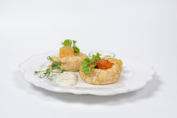  Top view Elegant crepes with red caviar and greens on white plate.