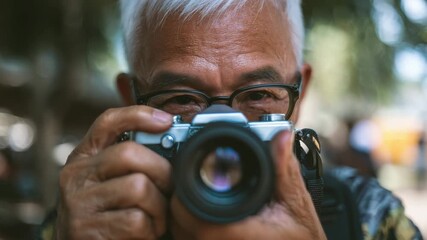 Lifelong learning attitude inspires elderly man with glasses capturing moments using vintage camera outdoors focused photography
