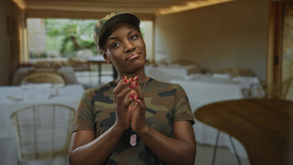 Soldier woman in camouflage uniform presses fingertips together at chest in restaurant interior;...