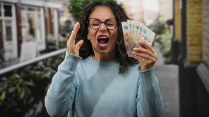 Woman smiling and holding argentine pesos outdoors on a city street, showcasing financial success...
