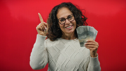 Woman holding indonesian rupiah banknotes and pointing upward against a vibrant red background,...