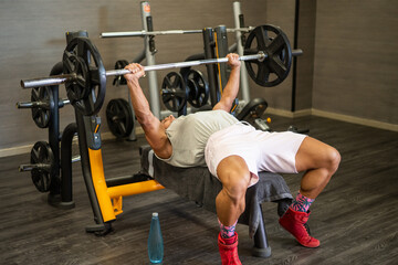 Muscular man performing a bench press exercise at the gym, strengthening chest and arm muscles as part of a dedicated fitness and bodybuilding lifestyle