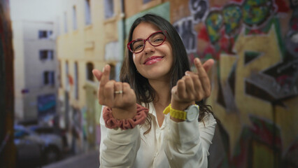 Young smiling woman making finger heart gesture on vibrant graffiti street outdoors; affection friendship.