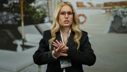 Woman gesturing on cruise ship deck with identification badge, blonde hair, professional attire,...
