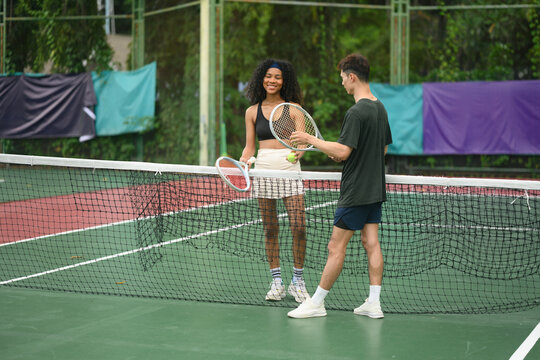 Multiracial friends enjoying a tennis session on a colorful outdoor court, showcasing teamwork, fitness, and fun