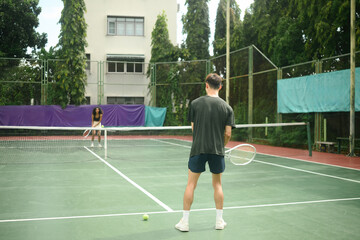 Fototapeta premium Tennis rivalry scene featuring an African woman and Asian man standing ready for a match on a green court