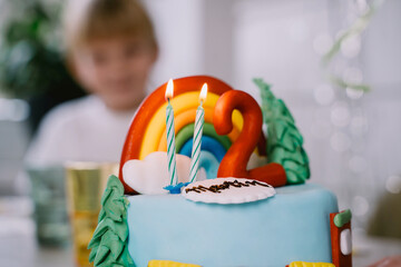 Birthday cake! Little boy celebrates his second birthday at home with his family. The children enjoy the festive birthday celebration in beautifully decorated kitchen. Retro-style photo with flash.