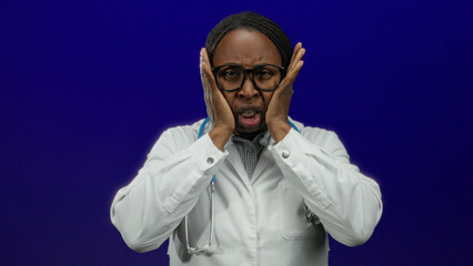 Woman doctor wearing glasses and white coat holds head in stress against blue background medical pressure concept