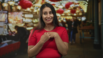 Woman holding paper heart to chest on a market street, smiling and clutching the heart with both hands; warm affection.