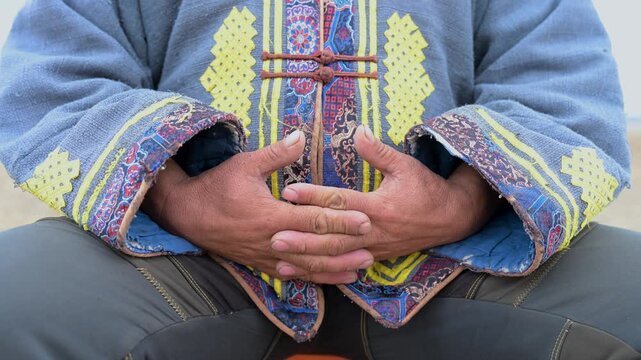 A close-up on the weathered hands of a nomad man as he talks. His expressive gestures highlight the intricate details of his traditional Mongolian deel.