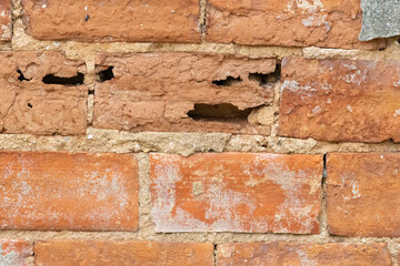 Weathered red brick wall with cracks and holes