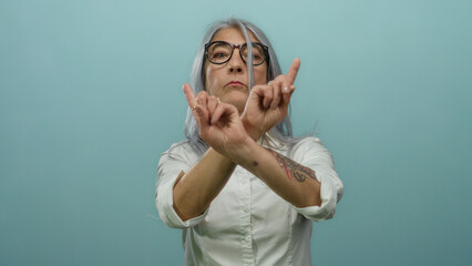 Senior woman with grey hair gesturing no with her fingers against a blue background, asserting a...