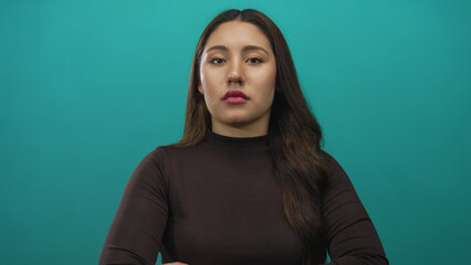 Obraz premium Young hispanic woman wearing a black top with arms crossed and gazing sideways in studio with teal background; rejection.