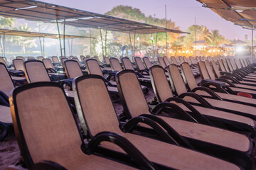 Rows of empty beach loungers arranged under canopy shades on a sandy beach at dusk, with soft lighting and a relaxed resort ambiance.