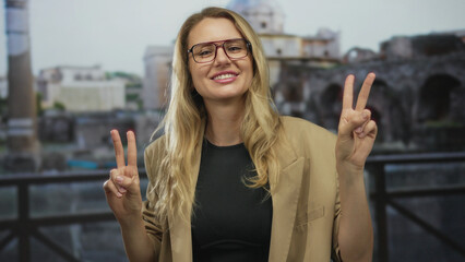 Fototapeta premium Woman smiling with peace sign in roman ruins, wearing glasses and beige blazer, depicting carefree travel mood in historic architectural setting outdoors showcasing cultural heritage.