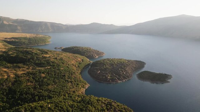 Drone aerial view of Nemrut volcanic crater lake in Bitlis Turkey with small green islands, blue freshwater, volcanic mountain slopes, lush vegetation, natural wonder, geology, tourism, travel
