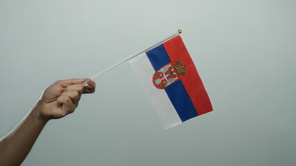 Serbian man holding a flag with a white wall background, showcasing serbia's colors in an isolated...