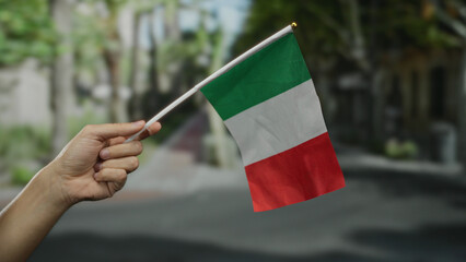 Hand holding italian flag outdoors on city street symbolizing national pride and cultural identity...