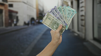 Caucasian man holding indian rupee banknotes outdoors on a city street, emphasizing the concept of...