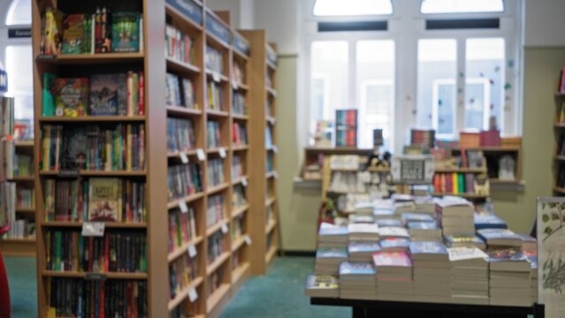 Defocused view of a library's vibrant aisles filled with colorful books and textbooks, offering an inviting indoor setting for literary exploration and reading pleasure.