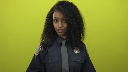 Young hispanic woman in police uniform gesturing confidently against a vibrant yellow isolated...