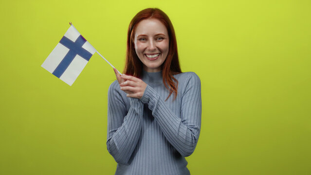 Woman holding finnish flag cheerfully against vibrant yellow background, embodying national pride and joyful expression.