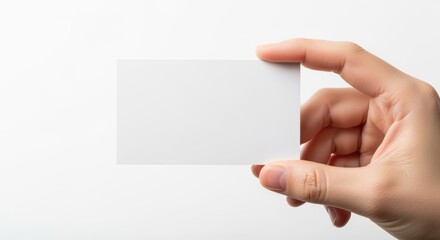 Obraz premium Hand holding blank white business card against clean white background. Perfect for mockups, branding presentations, and corporate identity designs. Fingers delicately grip empty card template.