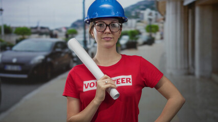 Obraz premium Young blonde woman architect wearing hardhat and glasses holding blueprint on street; confidence ambition planning.