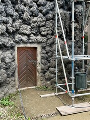 Reconstruction. A wooden door in a lavastone wall, with scaffolding nearby for ongoing maintenance or construction