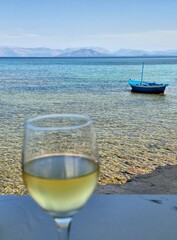Glass of white wine on a table in front of transparent, blue sea with small boat in the background