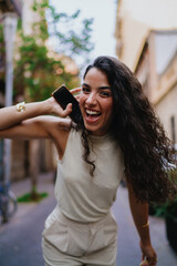 Naklejka premium Laughing woman bends toward camera with phone in hand, expressing vibrant joy and authenticity, capturing emotional presence and digital spontaneity.