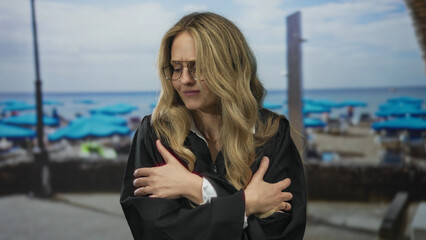 Woman crosses her arms shivering on a beach while young blonde judge in uniform watches the seaside outdoors.