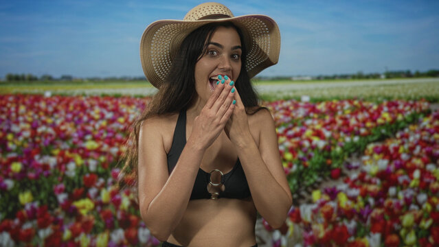 Woman in black bikini top and straw hat covers mouth with hand in forest; joy surprise wonder curiosity.