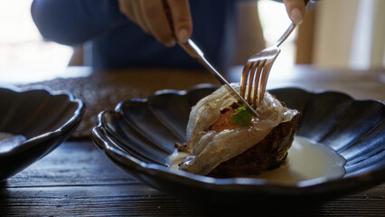 Close-up showing woman using fork and knife on gourmet dish indoors at mediterranean restaurant.