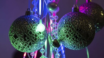 Hanging ornamental spheres with intricate glitter patterns illuminated by colorful green blue and purple lights with crystal-like bead strands - Powered by Adobe
