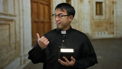 Priest holding bible stands in a church corridor with a confident expression