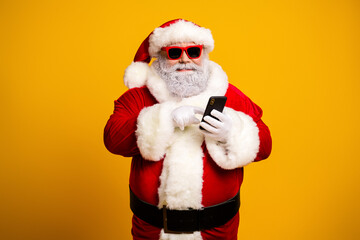 Funny Santa Claus with sunglass using smartphone on yellow background during Christmas season