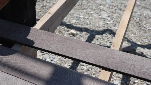 Deck Construction Installation fitting dark grey composite deck boards outdoors over gravel