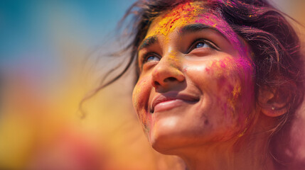 Close-up of a woman’s face coated in vibrant Holi powders, her upward gaze conveying joy, freedom and unity at the spring color festival.