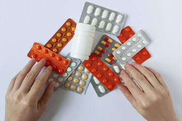 Tablets in an orange and silver blister pack, a medicine bottle. Hands of a Caucasian woman on medicine packaging. White background.