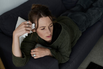 Obraz premium Young woman struggles with feelings of sadness while lying on her couch at home