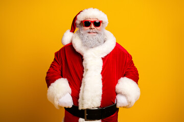 Santa Claus posing in festive red costume and sunglass on yellow background in celebration of the Christmas season