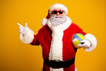 Santa Claus in a funky red costume holding a volleyball, smiling confidently and making a pointing gesture with a cool attitude