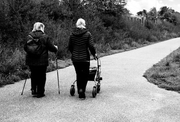 Elderly people taking a walk with help of walker with friends on a cold day through the park