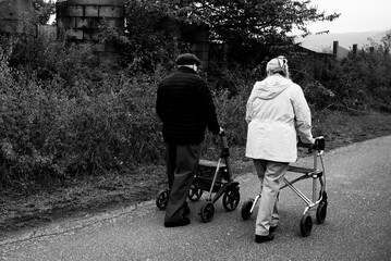 Elderly people taking a walk with help of walker with friends on a cold day through the park