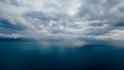 Fototapeta premium Moody seascape with storm clouds and rain over the ocean. Dark clouds hang low above the calm sea, creating a dramatic and atmospheric coastal view.