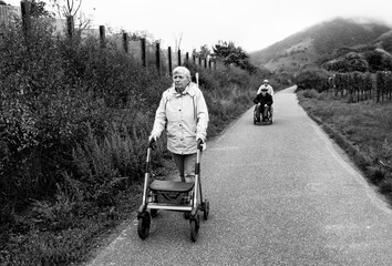 Elderly friends taking a walk in the park during cold weather with help of wheelchair and walker enjoying and having fun